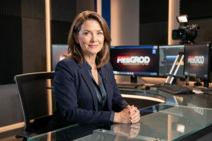 Présentatrice TV française en blazer marine assise au bureau d'un plateau de journal télévisé avec moniteurs et caméras en arrière-plan